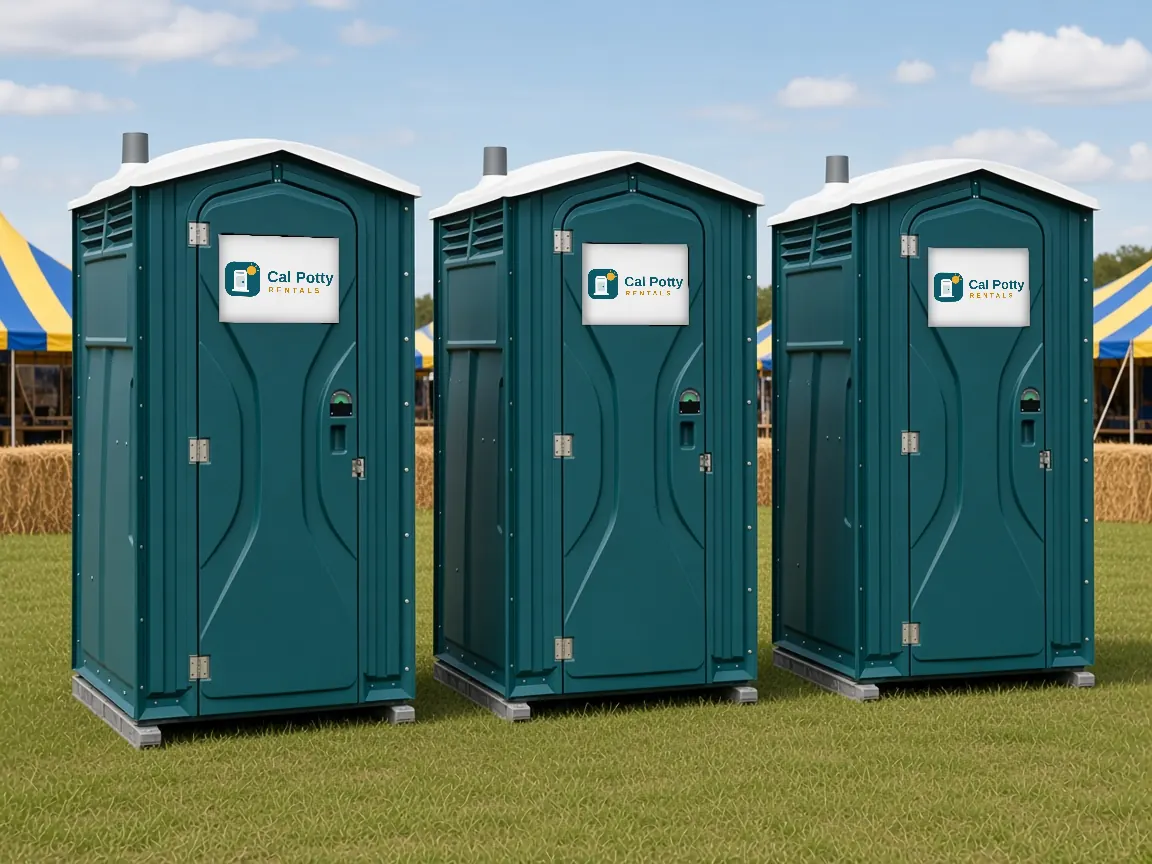 Three teal portable toilets on grass at a community fair with striped tents behind